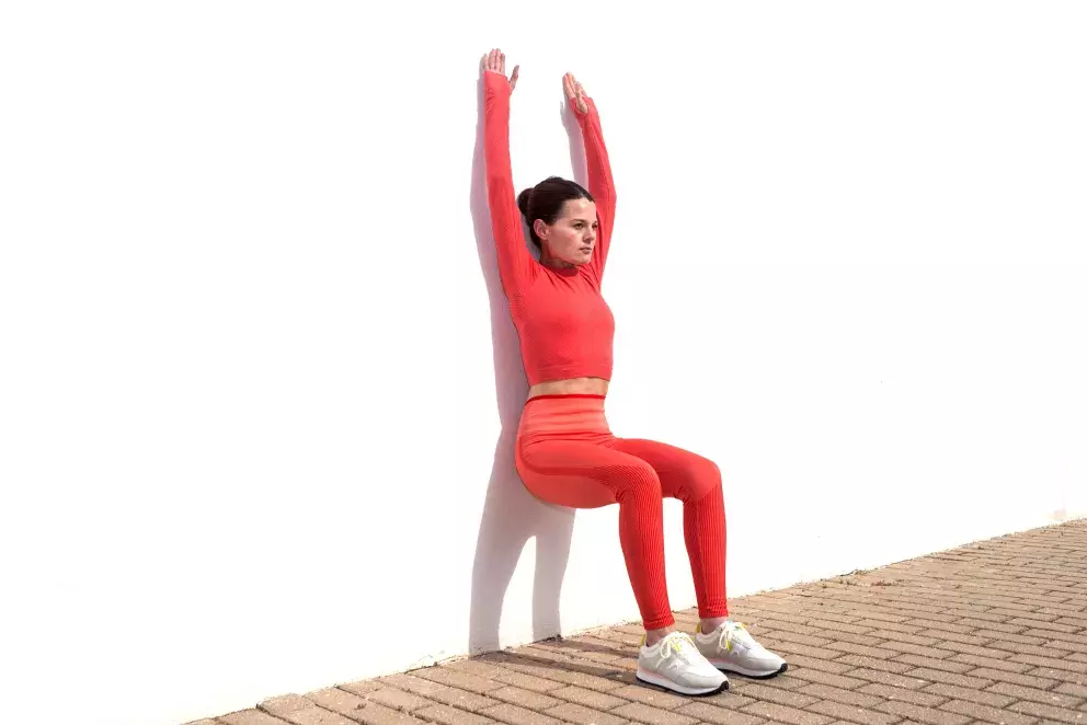 <p>Dřep o zeď provádíme opět klidně i několikrát denně. <strong>Postavte se zády ke zdi a pomalu se posuňte do pozice dřepu</strong>. Záda a hlava se musí celou dobu dotýkat zdi. Nohy pomalu posouvejte od stěny tak, abyste vytvořili základní pozici dřepu – kolena by měla být ohnutá pod úhlem 90°, prsty směřují dopředu a stehna jsou rovnoběžně s podlahou. Postupně můžete přidávat ruce a měnit pozice nohou. </p>
