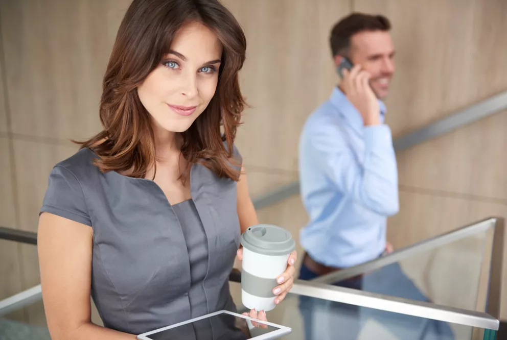 žena s kávou a tabletem, muž za ní