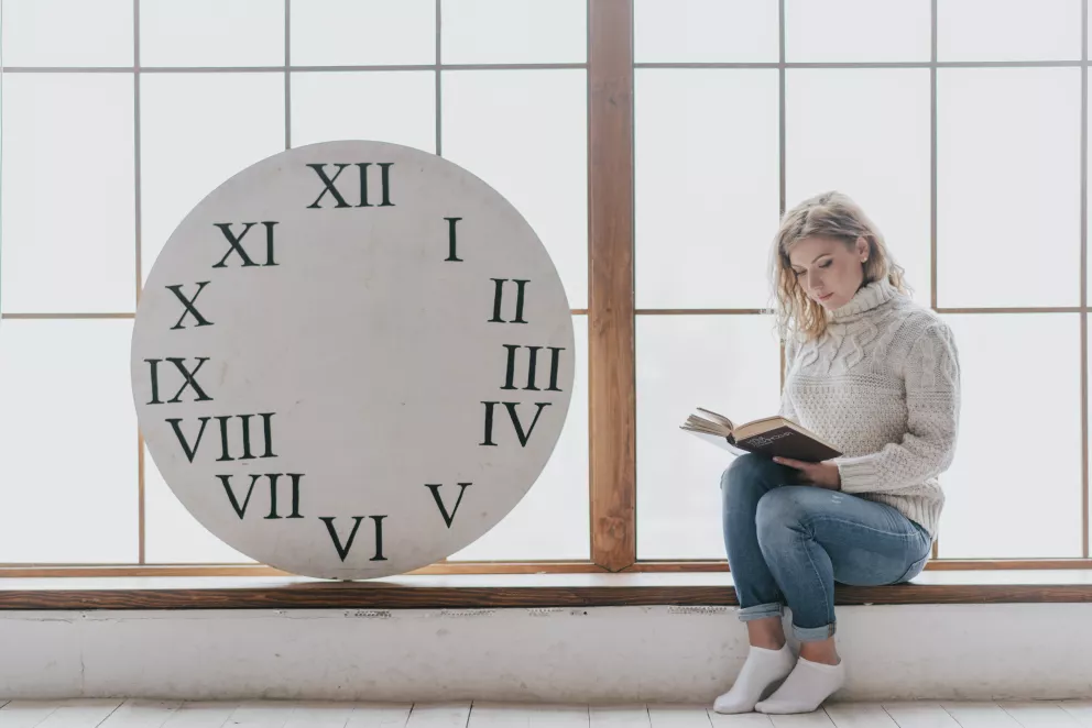 žena si čte vedle hodin s římskými číslicemi