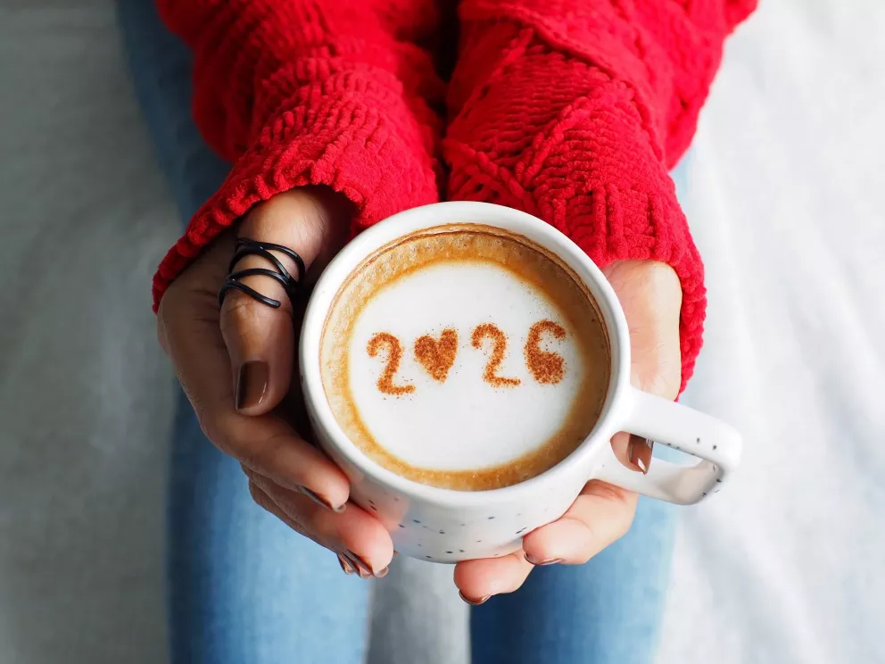 žena drží v ruce hrníček s kávou s číslovkou 2026 v pěně